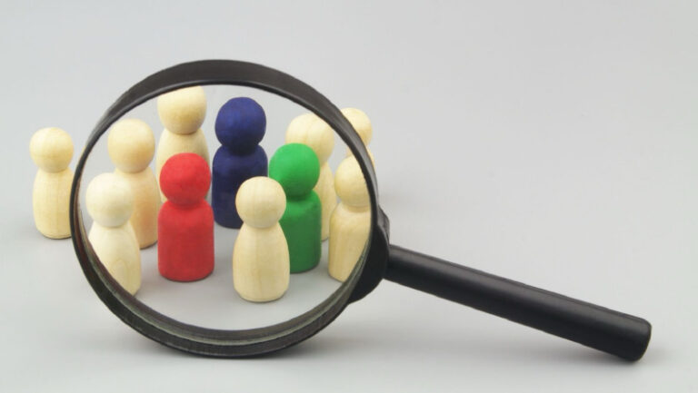 Group of not colored figures with few colored under magnifying glass on grey background. Choosing personnel and hire employers, HR and people recognition concept.